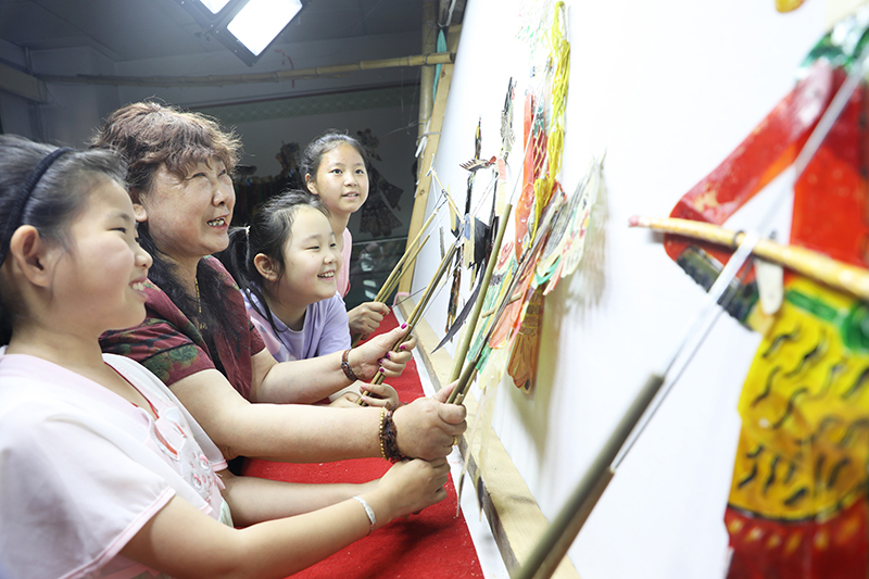 皮影藝人指導(dǎo)小朋友表演皮影戲。