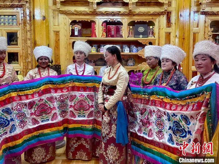 圖為女性展示村民自發(fā)繡制的“百米五彩哈達”。　李玉峰 攝